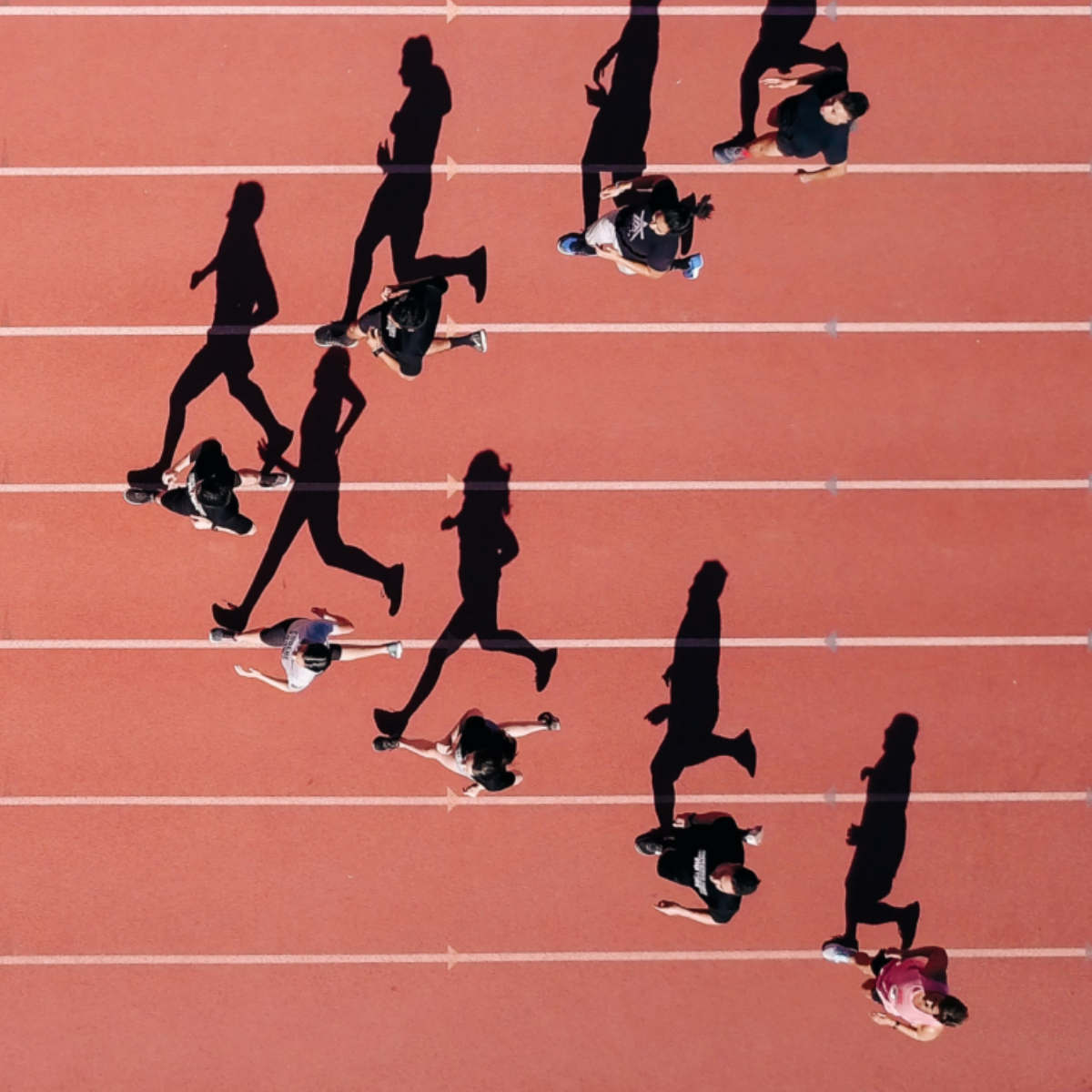 Folk løber på en athleticspored, og deres skygger kaster lange skygger på banen.