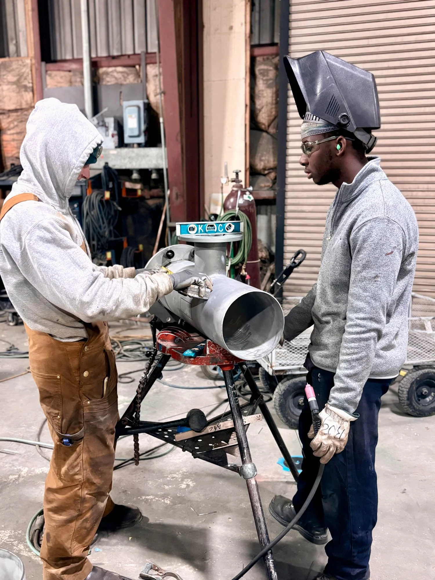 two men working on industrial pipe in a fabrication shop
