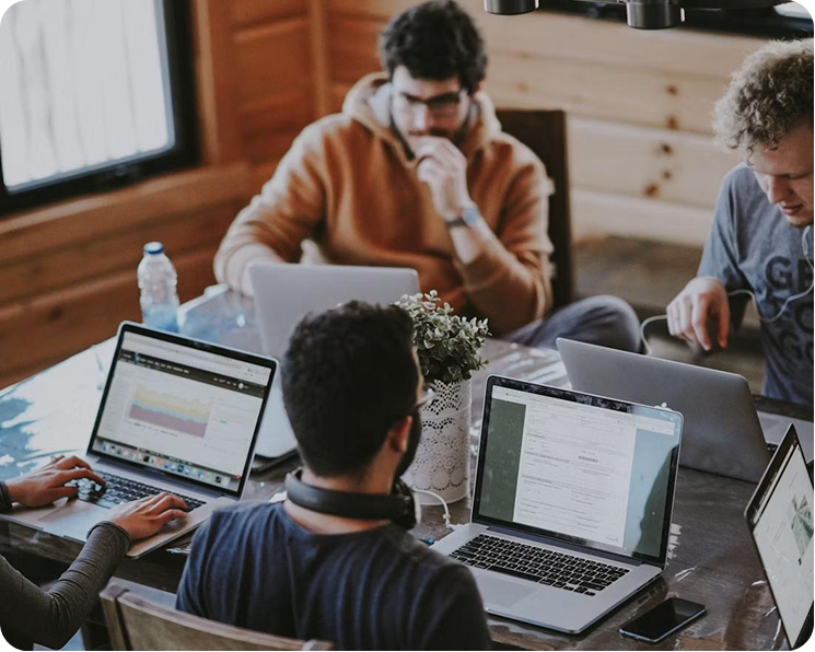 Four people working on laptops around a wooden table in a cozy, wood-paneled room.