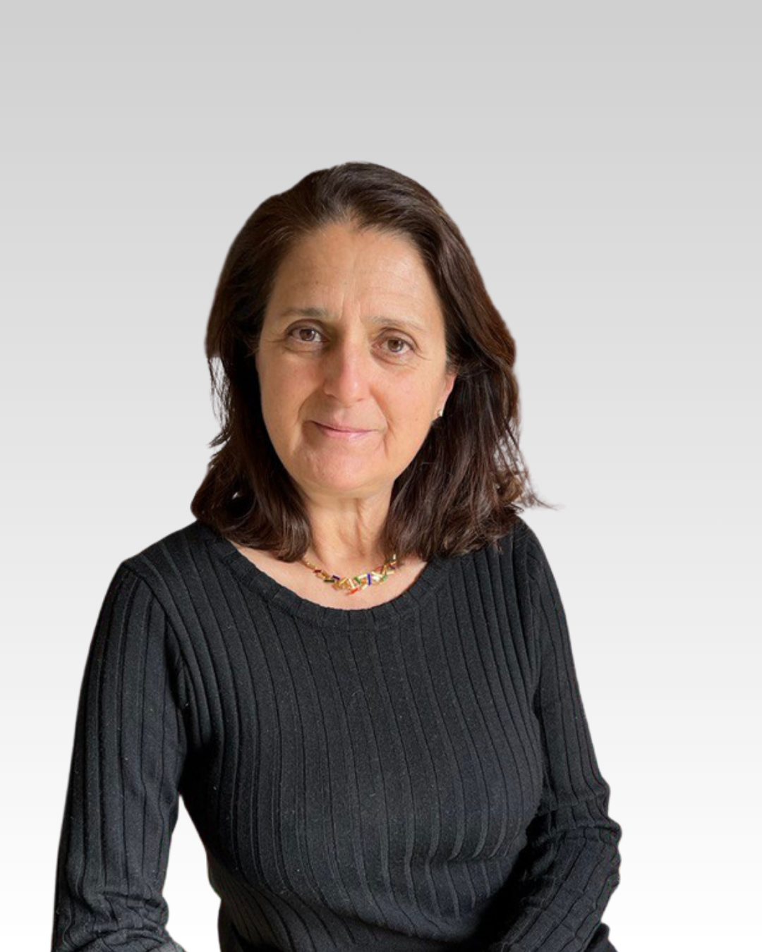 Una donna con capelli castani e corti, indossa una maglietta nera a righe e una collana colorata, sfondo grigio chiaro.