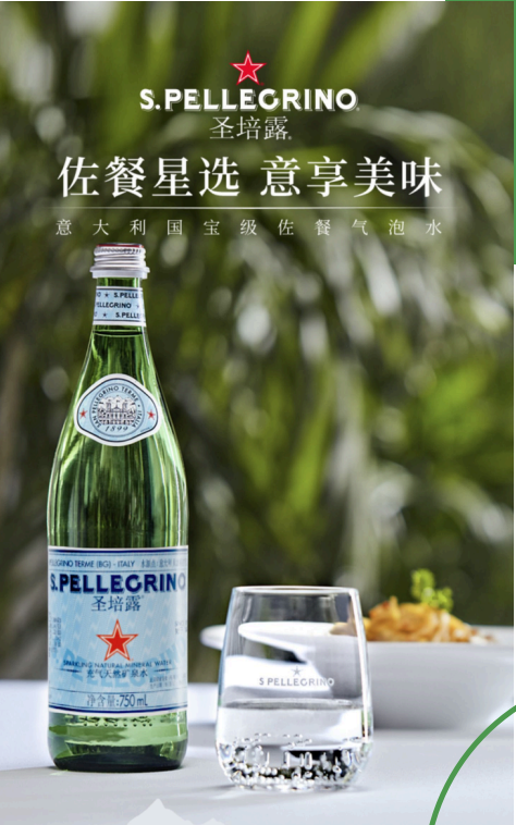 Bottiglia di acqua naturale S. Pellegrino e un bicchiere d'acqua su un tavolo con un piatto di cibo sfocato sullo sfondo, con uno sfondo verde di foglie.