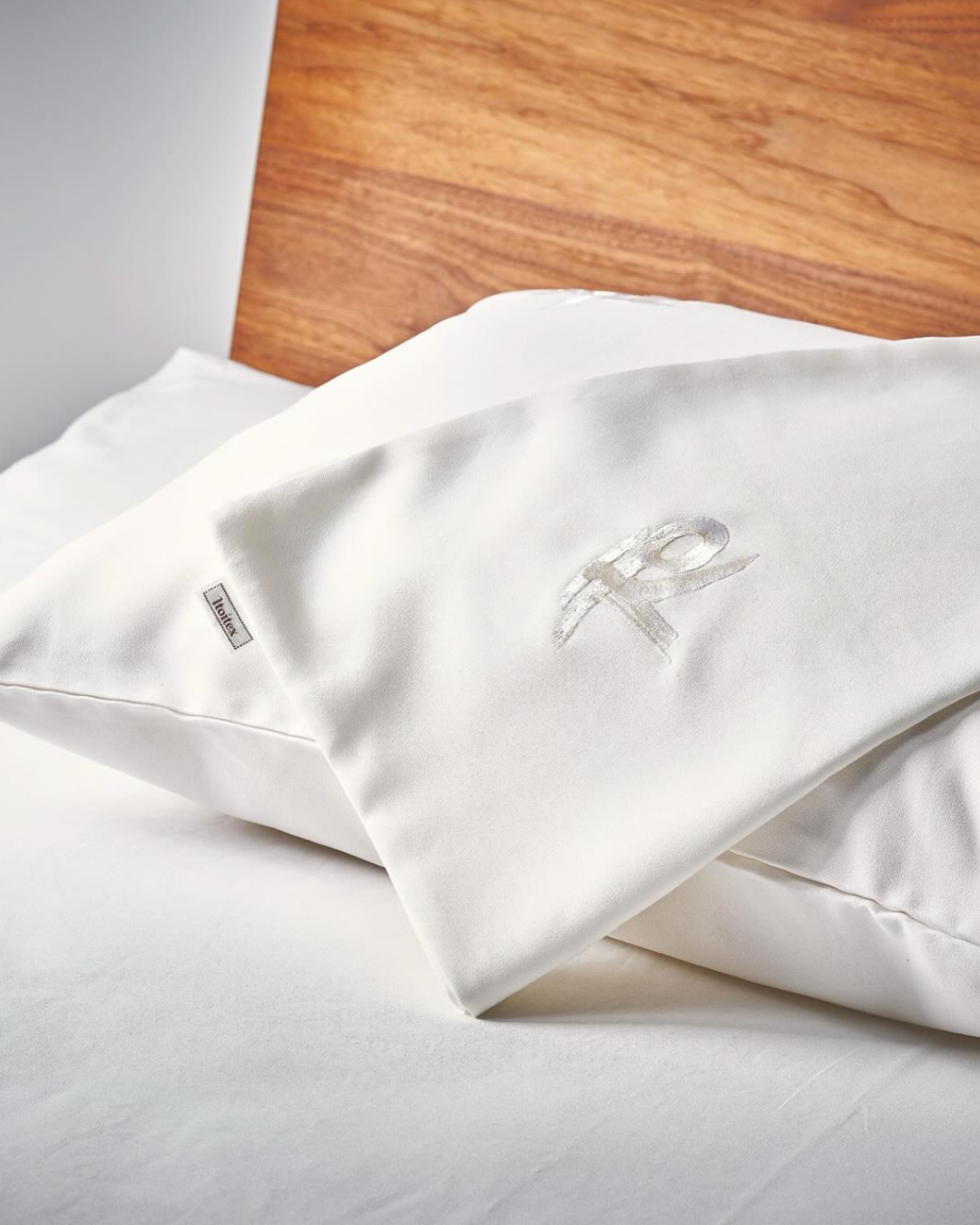 Cuscino e copriletto bianchi con ricamo color argento su letto vicino a parete di legno.