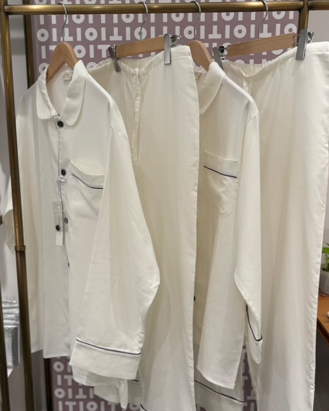 Page di pigiami in tessuto bianco con dettagli in nero, appesi a una rastrelliera.