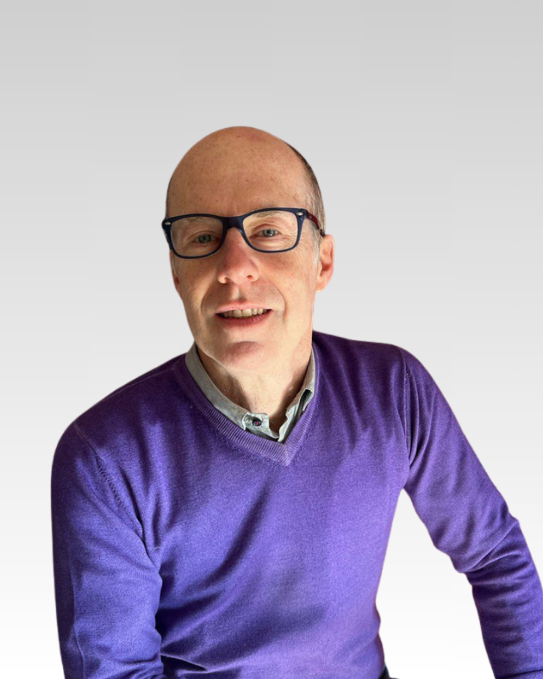 Uomo con capelli rasati, che indossa occhiali neri e una maglia viola, sorridente, sfondo bianco