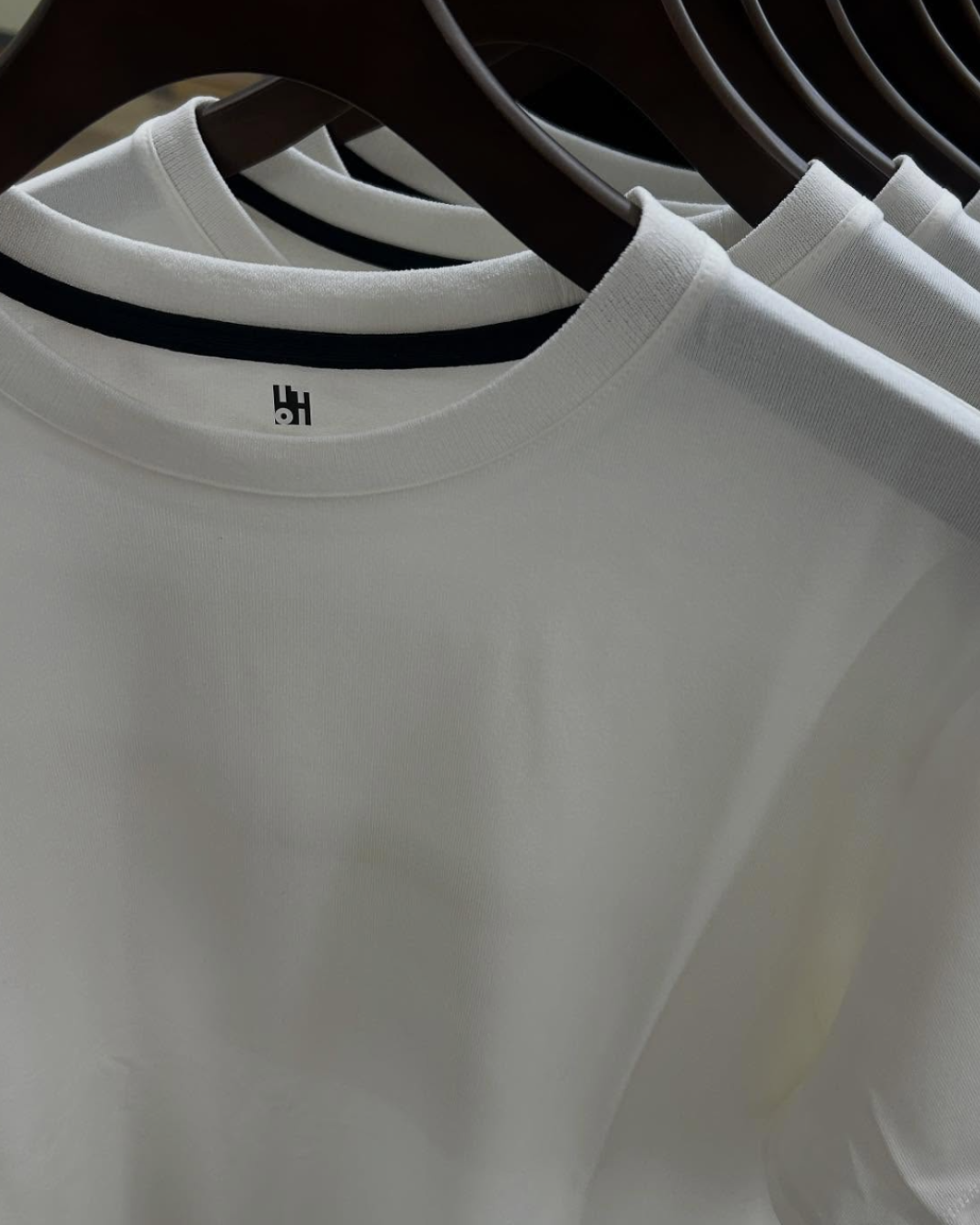 Magliette bianche con colletto tondo appese su cassettiere in bianco e nero