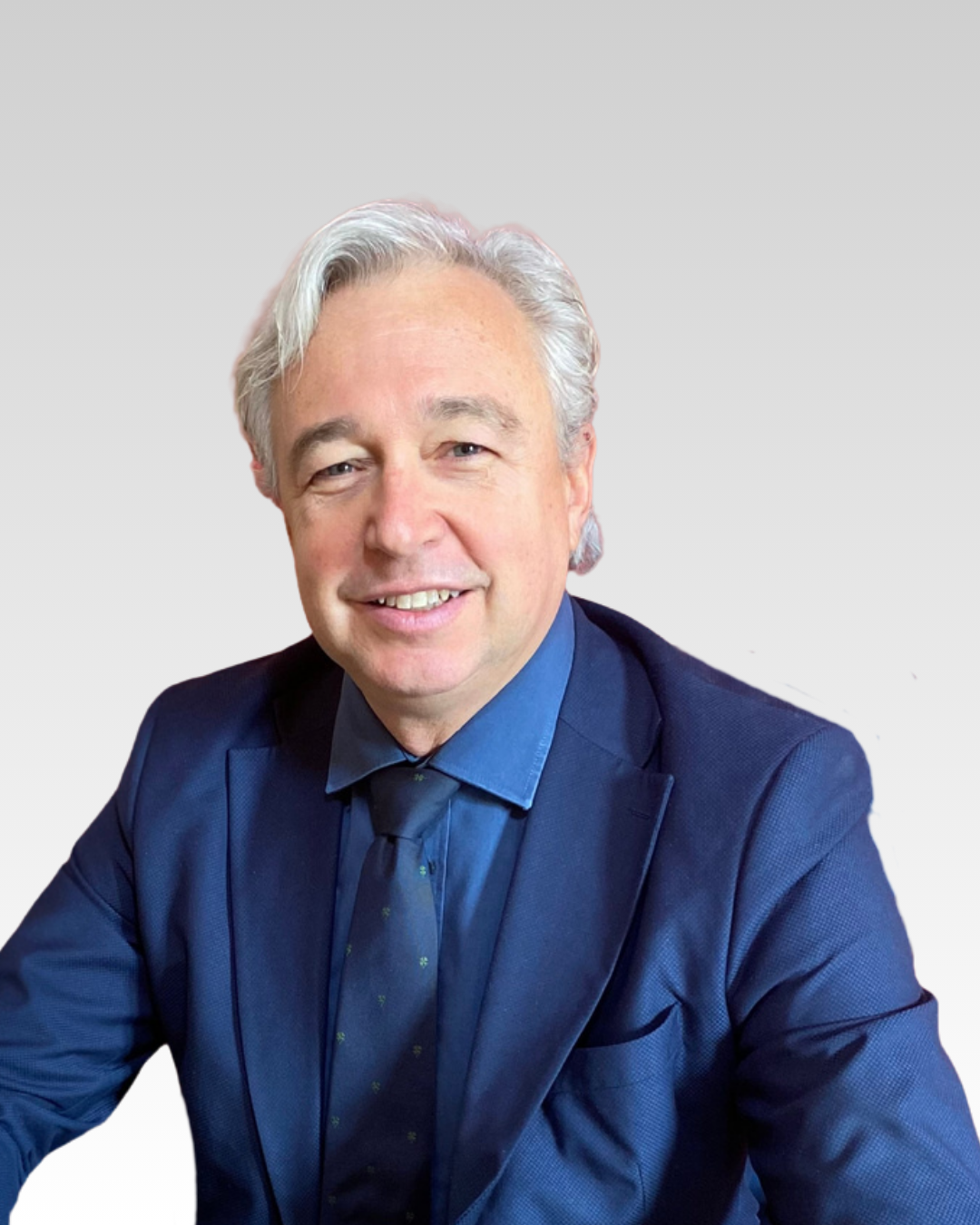 Uomo con capelli grigi all'esterno, indossa un completo blu e una cravatta con motivo a punti, sorride alla fotocamera.
