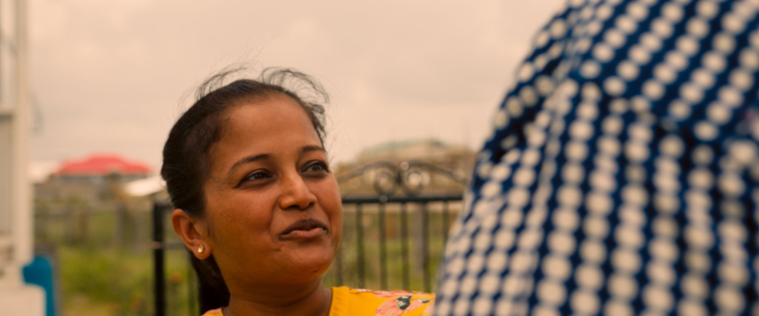 Close-up of a woman smiling and looking at another person in conversation, with a blurred outdoor background.