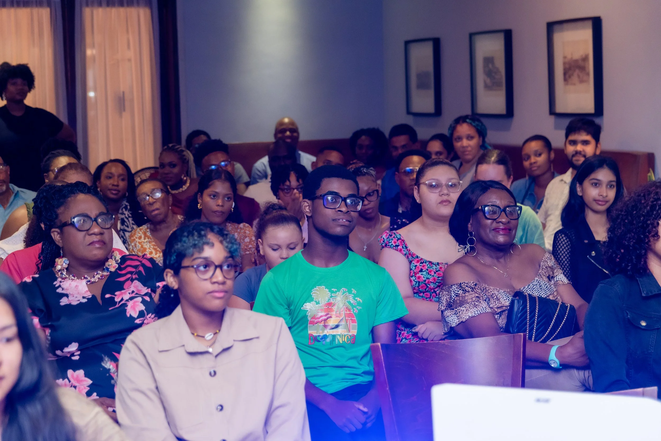 Audience of diverse men and women seated in a room watching a presentation or speech.
