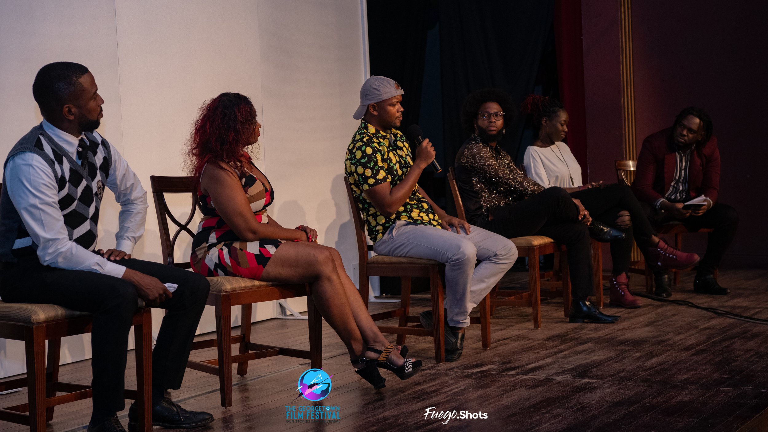 Six people sitting on stage in a panel discussion at a film festival, with one person in the middle holding a microphone.