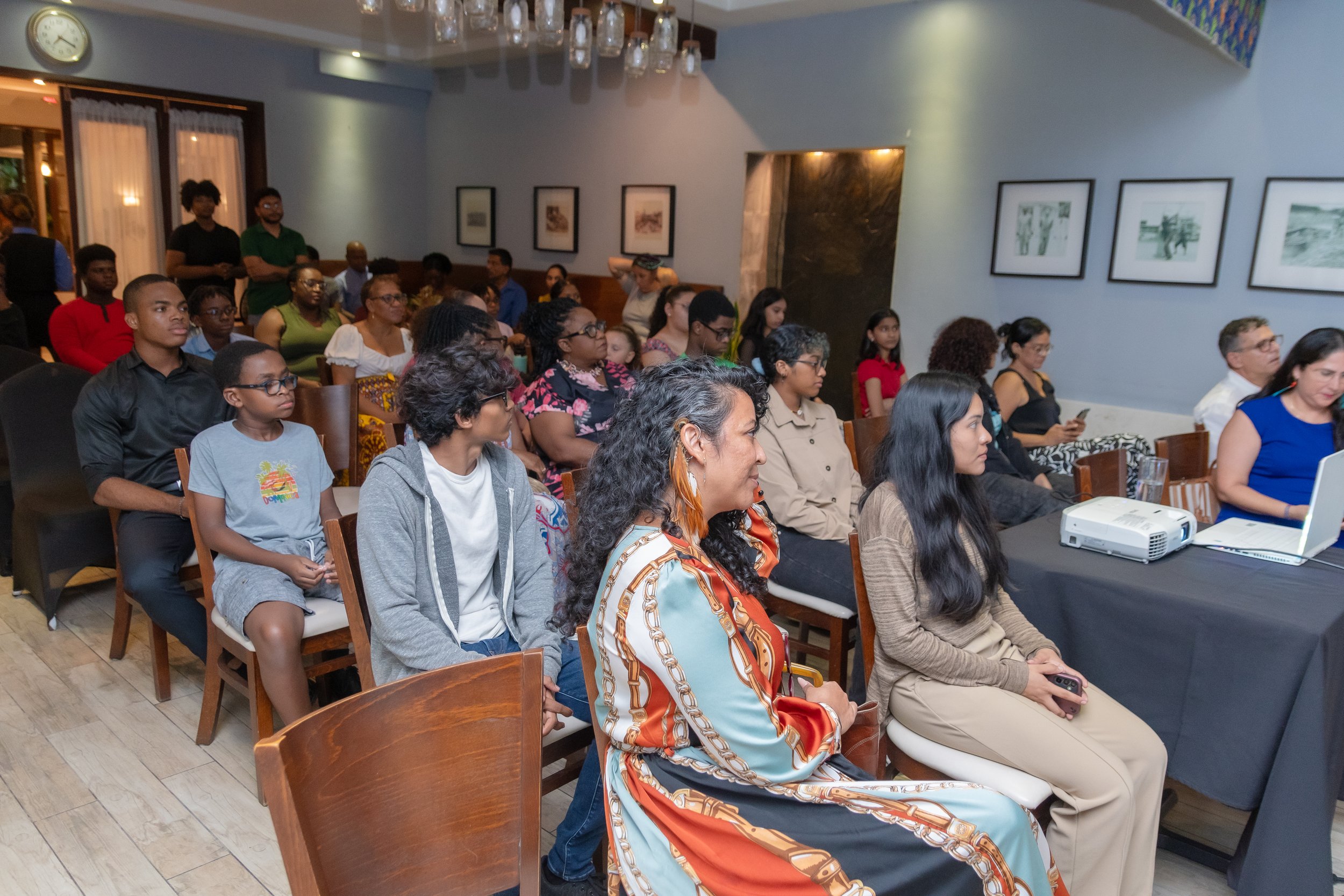 People attending a presentation or event in a restaurant or conference room, seated and watching attentively.