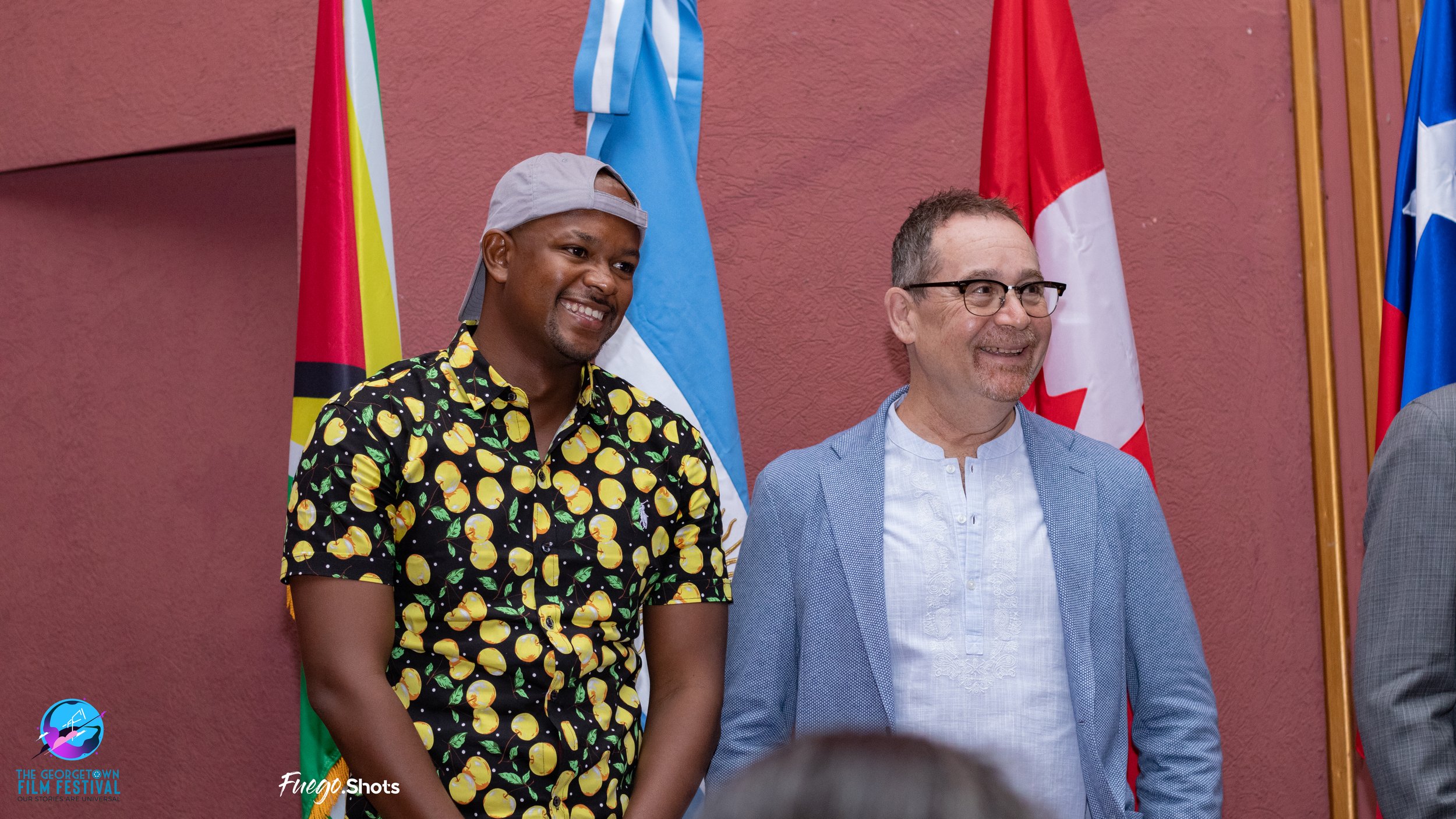 Two men standing side by side smiling, with flags in the background, at the Georgetown Film Festival.