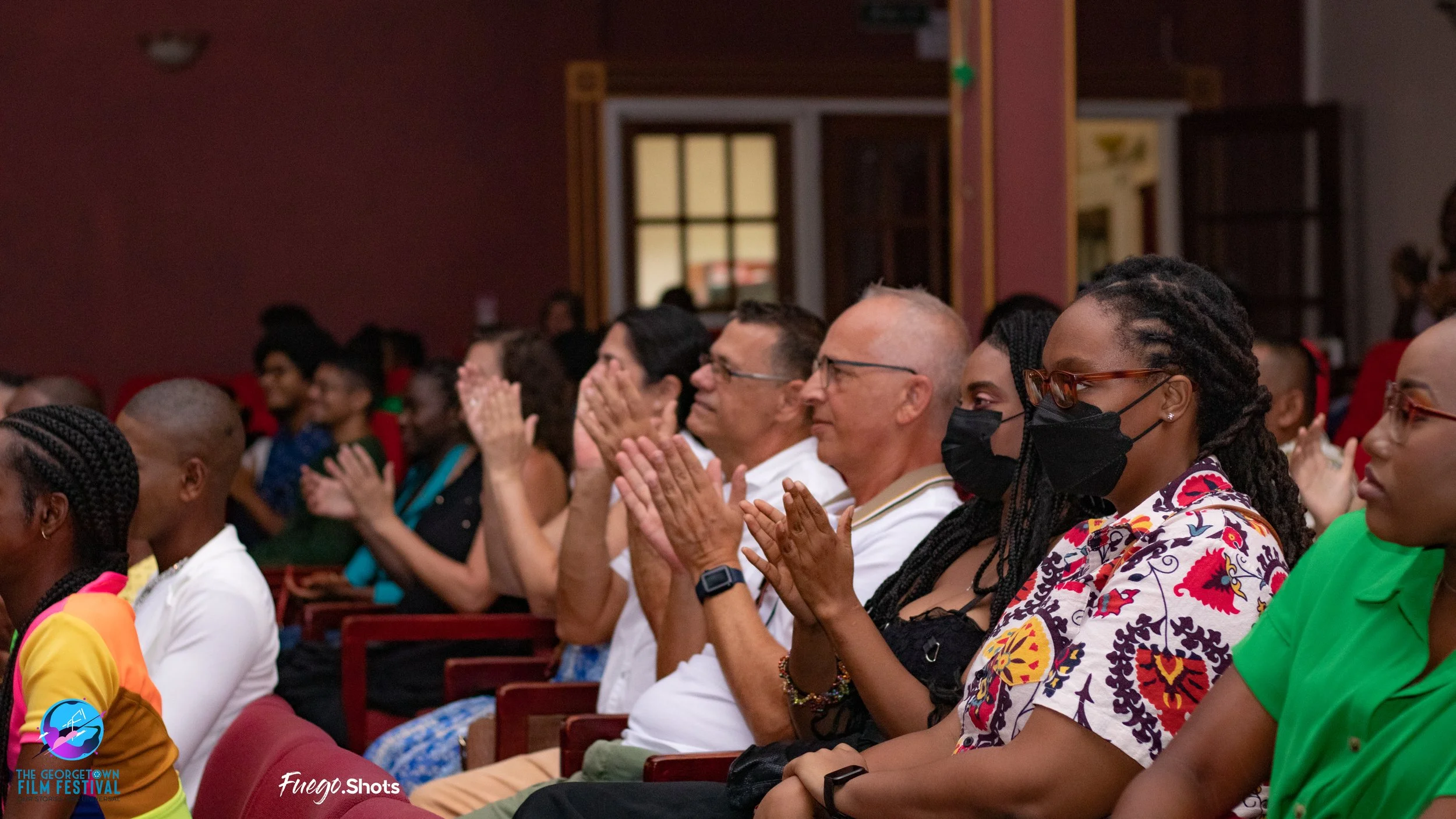 Audience attending a film festival, several people wearing masks, sitting in theater seats, clapping and watching a presentation.