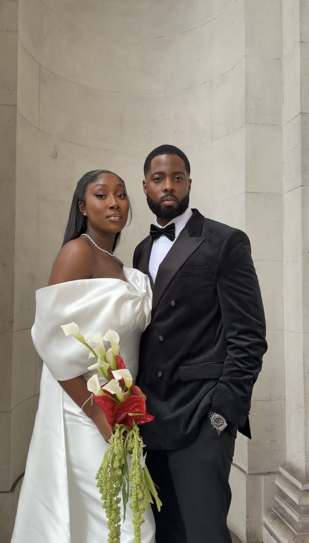 A bride and groom posing together in wedding attire in a stone building.
