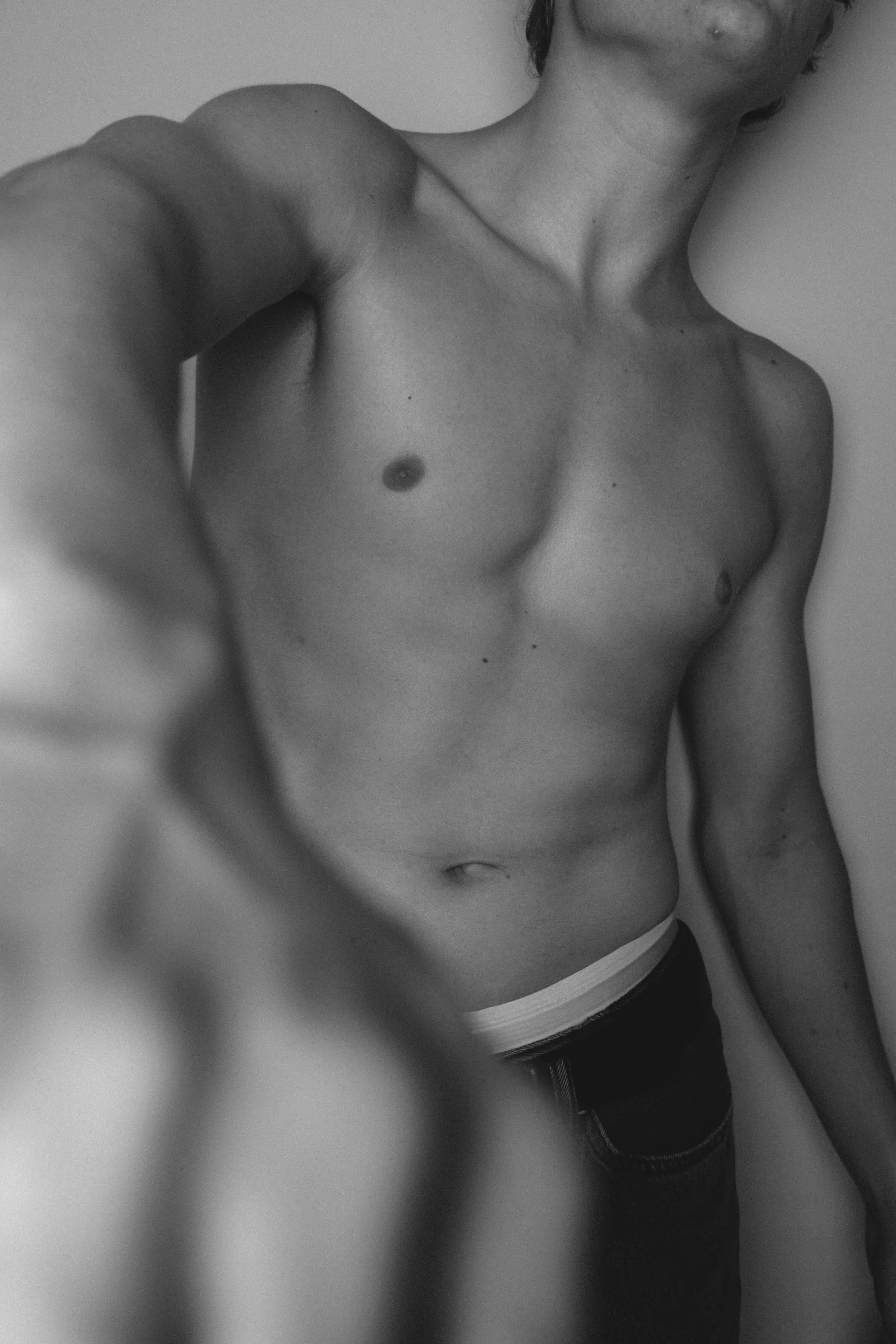 Black and white photo of a woman's upper body, showing her chest, neck, and part of her face, with her arm extended in front of her, possibly taking a selfie or in a mirror.