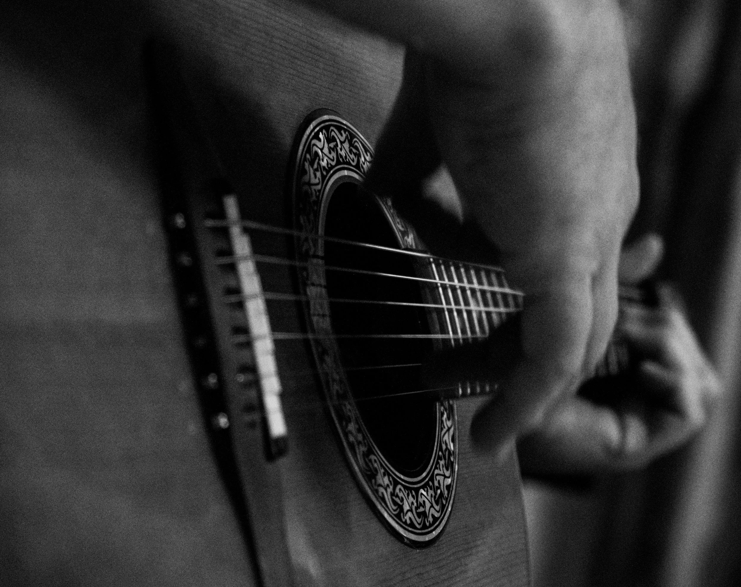 Close-up of an acoustic guitar in black and white, showing the soundhole and part of the body.