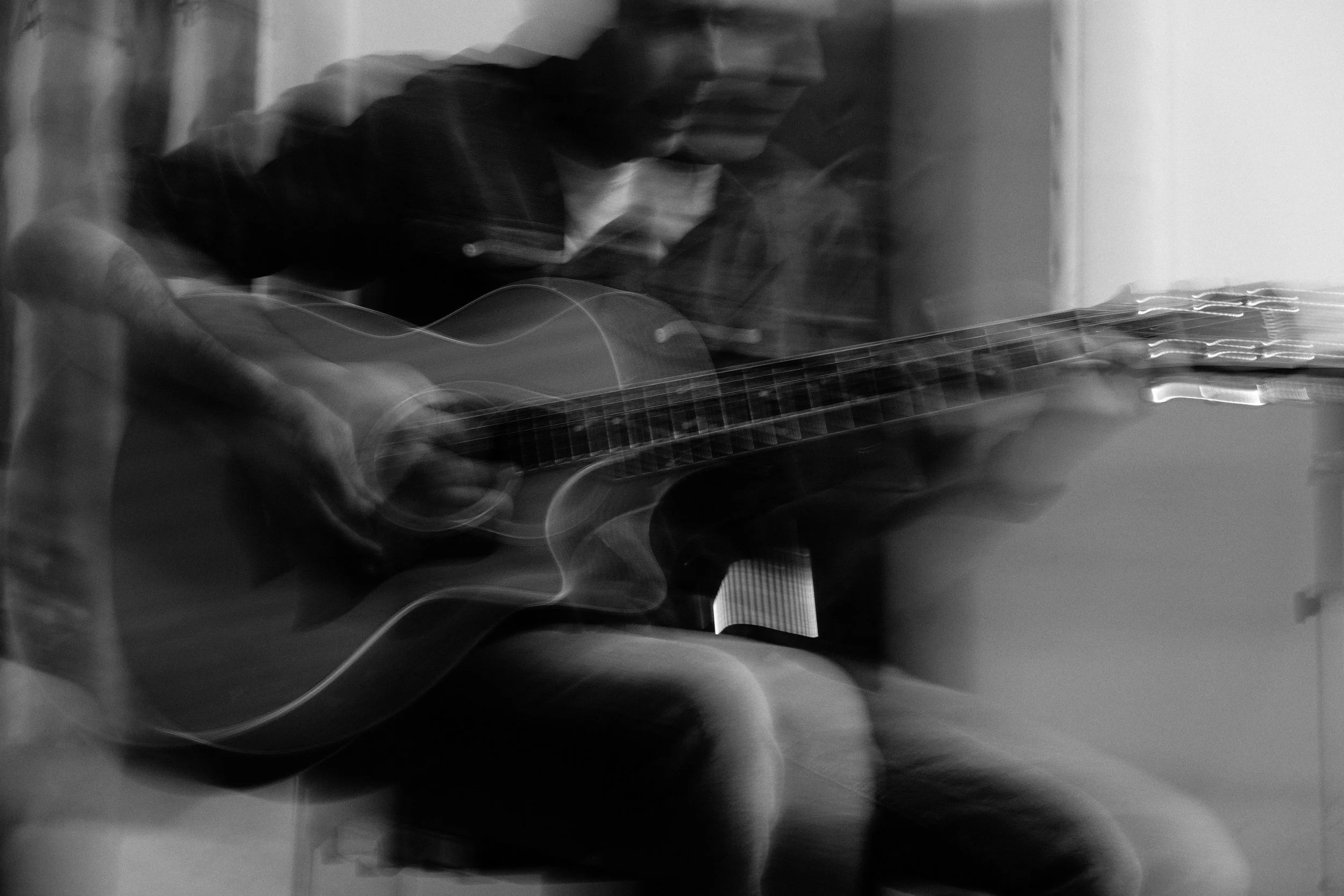 A person playing an acoustic guitar with motion blur, creating a dynamic, artistic effect in the black and white photo.