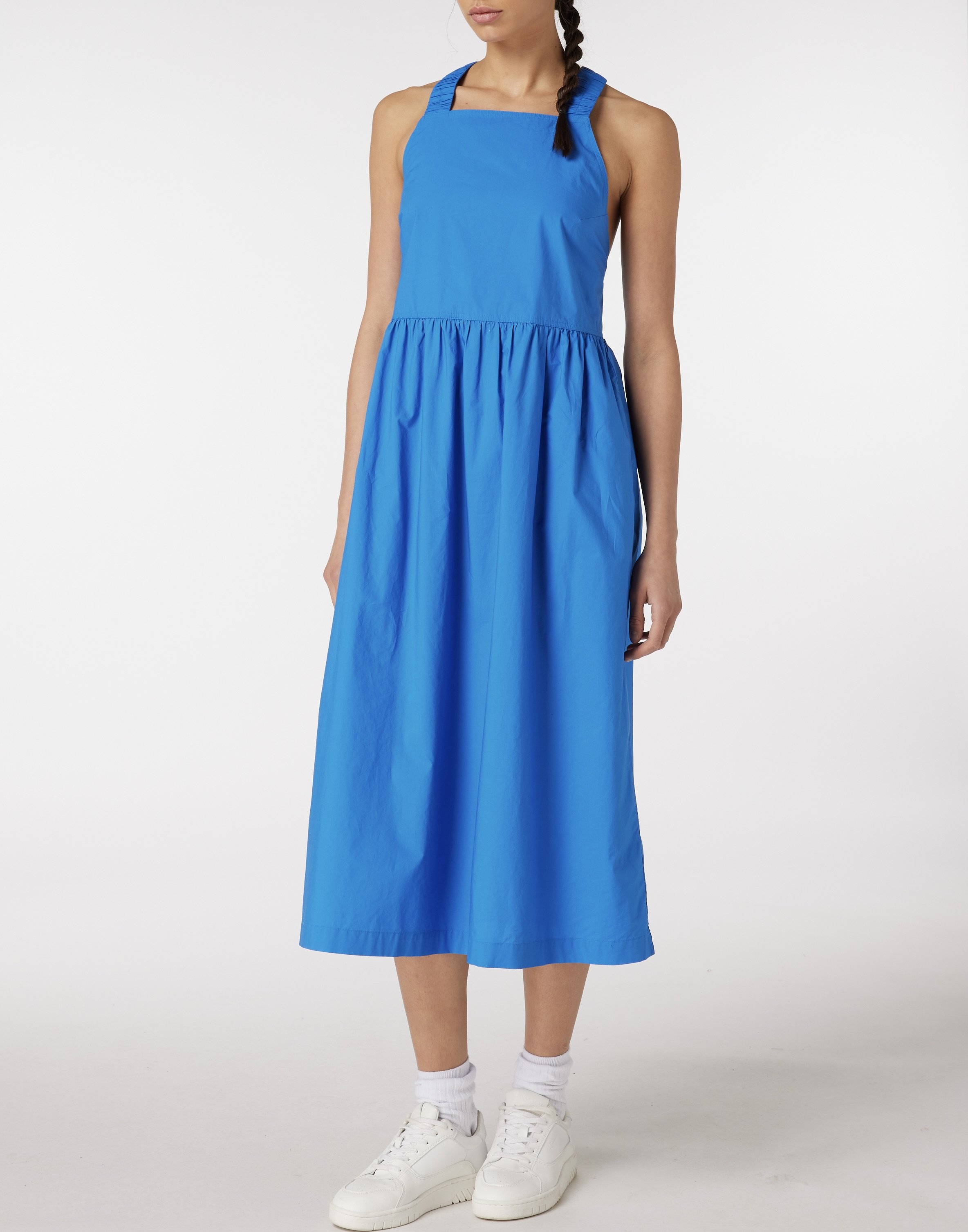 Woman wearing a blue sleeveless dress, white sneakers, and white socks, standing against a plain white background.