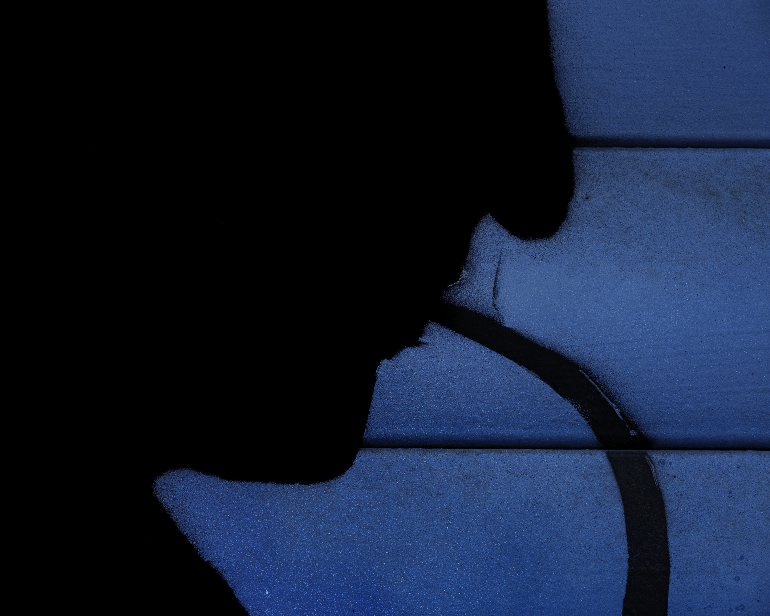 Silhouette of a person drinking from a straw against a blue-lit wall.