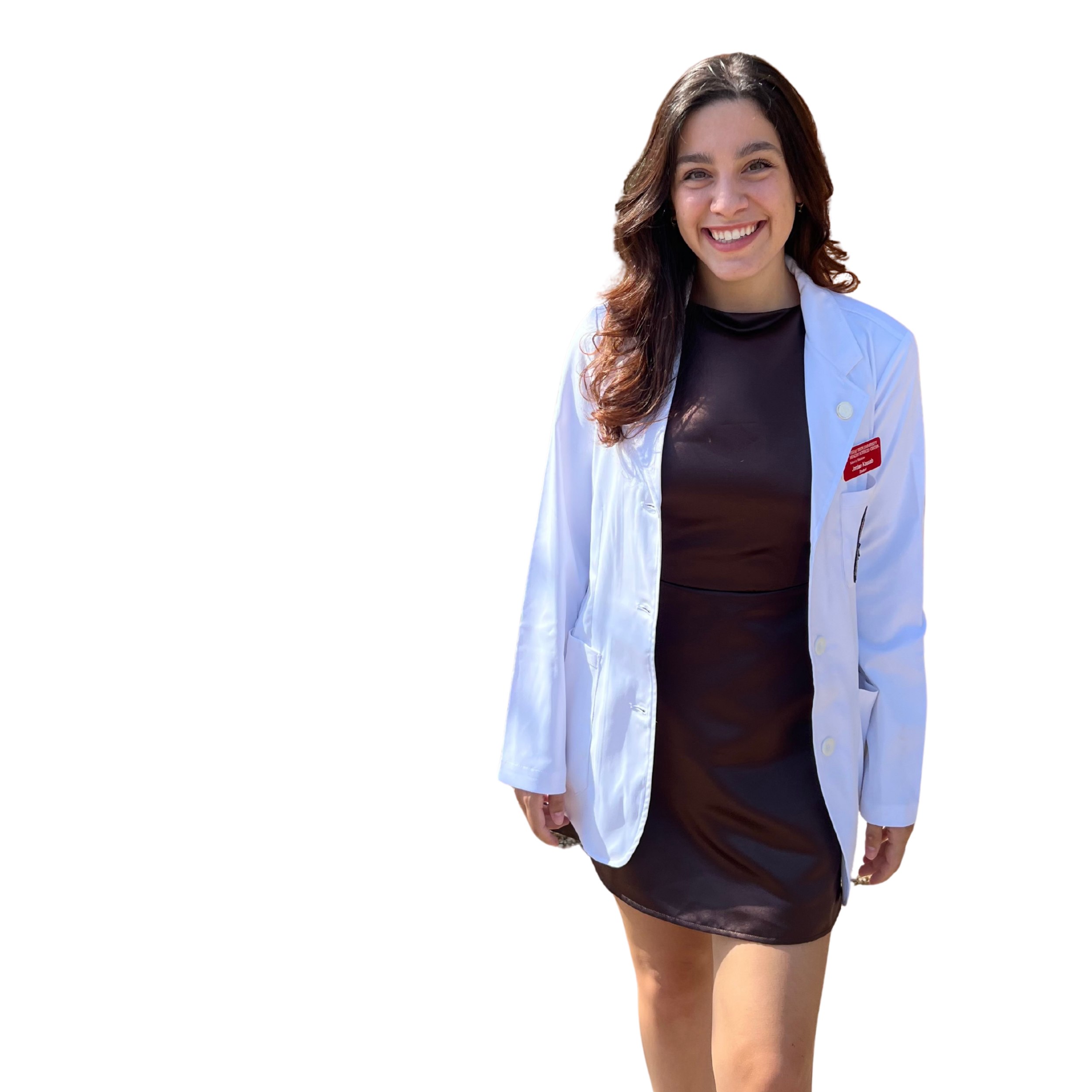 A young woman with long brown hair smiling, wearing a black dress and white medical coat, standing outdoors.