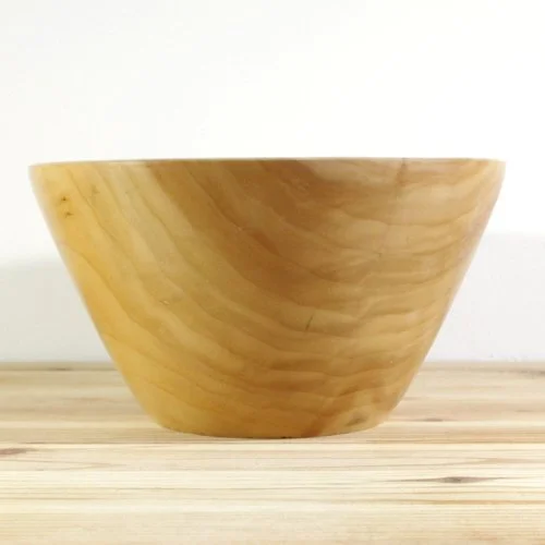 A wooden bowl on a light wooden surface with a plain white background.