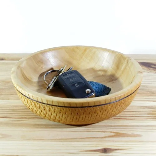 Wooden bowl on a wooden surface holding a car key with a black fob and a blue strap.
