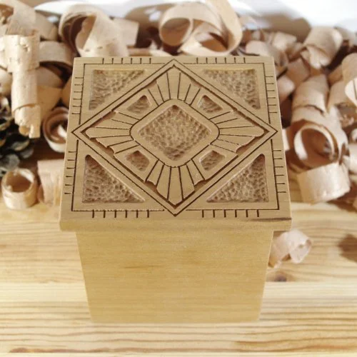 A wooden keepsake box with intricate geometric patterns, placed on a light wooden surface with wood shavings in the background.