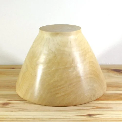 A wooden bowl turned upside down, showing the outside surface, resting on a wooden surface against a white background.