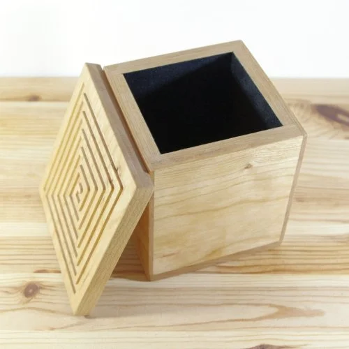 Wooden box with a removable square spiral lid, empty interior, placed on a wooden surface.