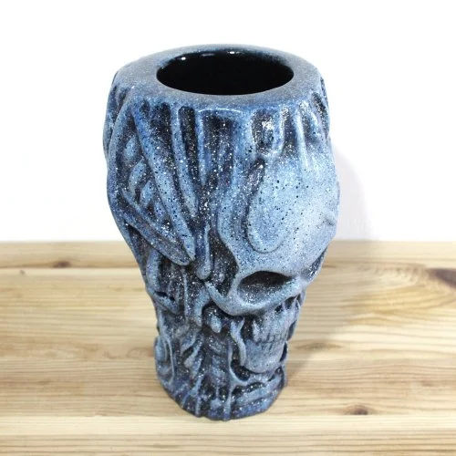 A blue and black skull-shaped vase with textured details, placed on a wooden surface.