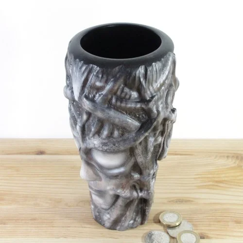 Gray and black textured wooden vase inspired by H.R.Giger, placed on a wooden surface with coins nearby.