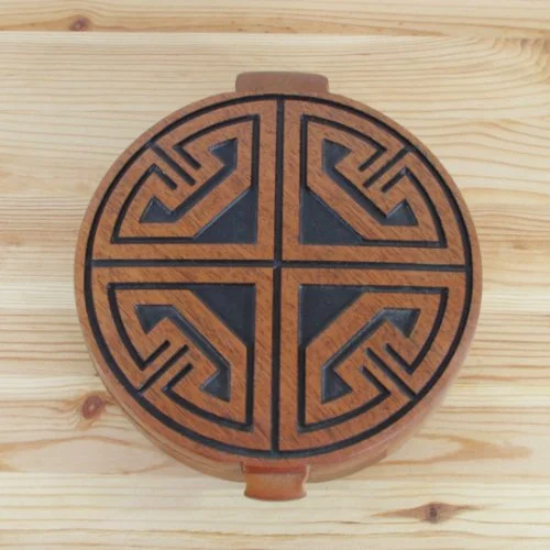Round jewellery box with geometric patterns on the lid, divided into four sections by black lines, placed on a light wooden surface.