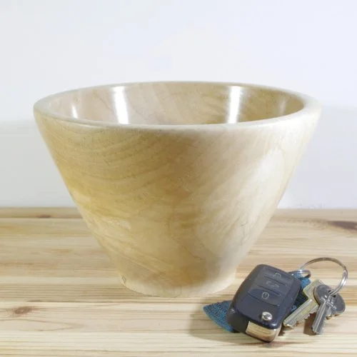 A beige ceramic bowl with a marbled pattern on a wooden surface, with car keys and a keychain beside it.