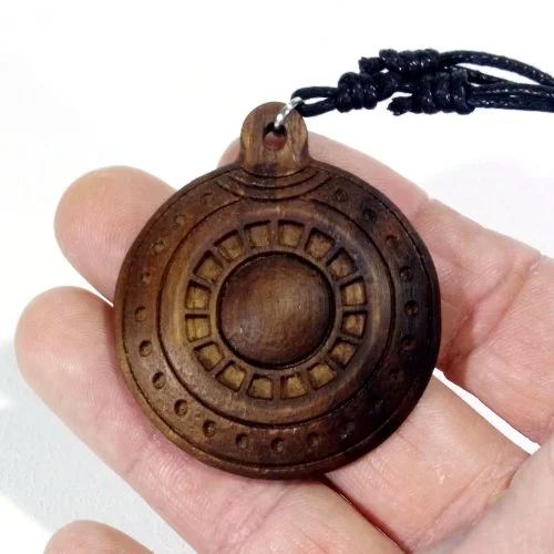 A person holding a round wooden pendant with a hole at the top, attached to a black cord, featuring carved circular patterns.