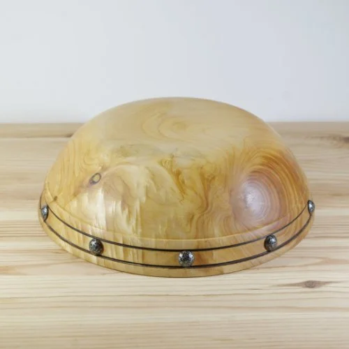 A wooden bowl with decorative metal stud accents sitting on a wooden surface.