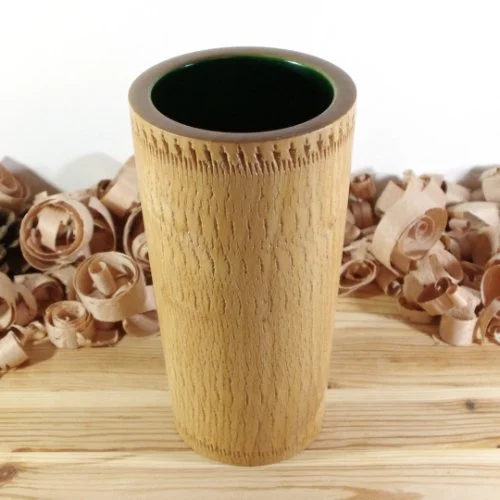 A wooden vase with a hollow center on a wooden surface, surrounded by wood shavings, with a white background.