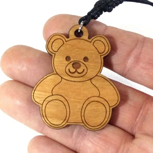 Wooden teddy bear pendant with a black string, held between fingers.