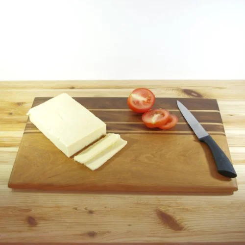 Blocks of cheese, halved cherry tomatoes, and a kitchen knife on a Maple and Walnut cutting board.