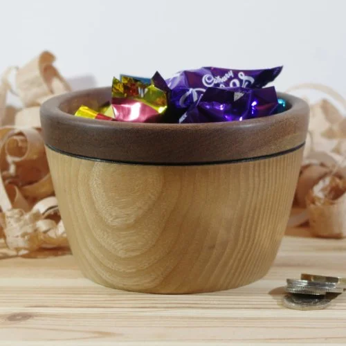 Wooden bowl filled with colorful wrapped candies on a wooden surface with wood shavings in the background.