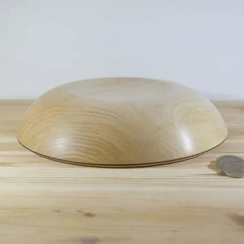 Wooden bowl with a curved shape placed on a light wooden surface, with a coin nearby for size comparison.