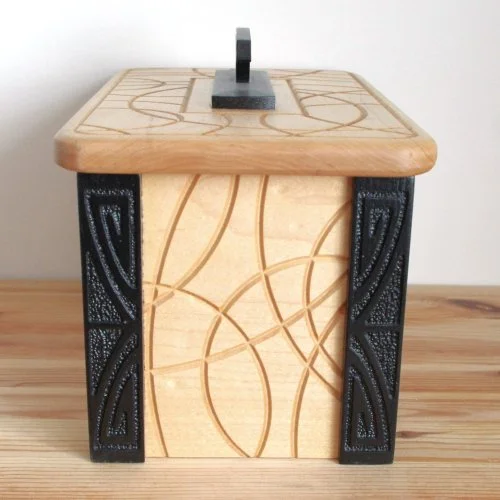 A wooden keepsake box with a black handle on top, decorative black sides.