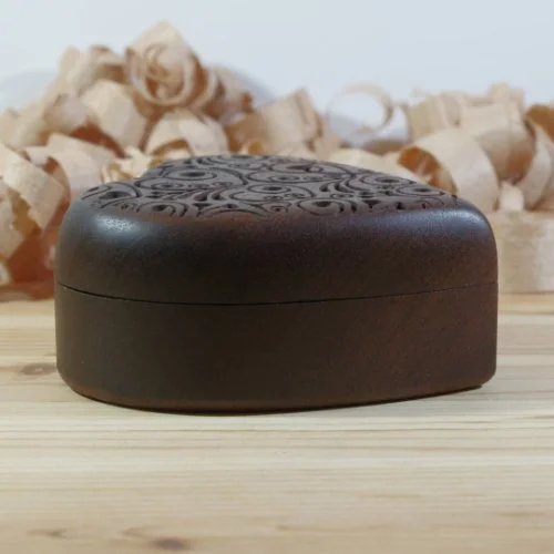 A decorative heart shaped box carved patterns, placed on a wooden surface with wood shavings in the background.
