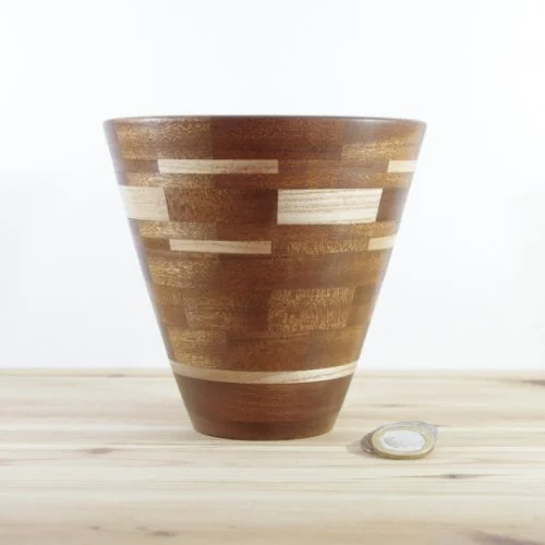 A handmade segmented wooden vase with a geometric design, placed on a wooden surface next to a small coin.