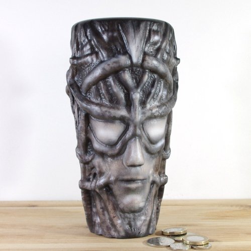 A wooden vase inspired by H.R.Giger, featuring intricate carvings, placed on a wooden surface with coins in front of it.
