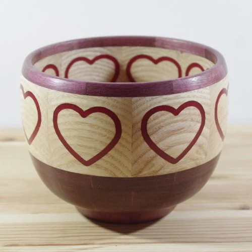 A wooden bowl decorated with red hearts around its exterior, sitting on a wooden surface.