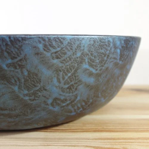 Close-up of a blue wooden bowl with a blue and gray pattern on a wooden surface.