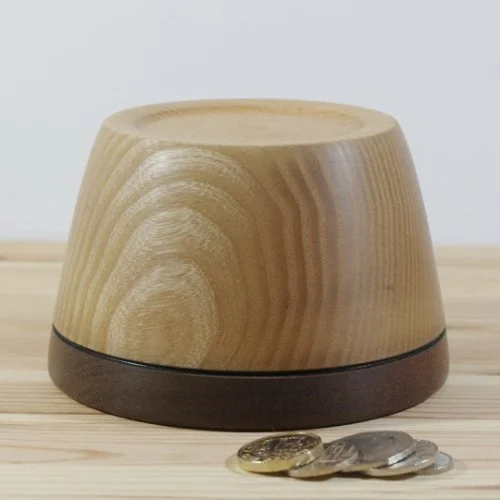 Wooden cylindrical container with a dark base placed on a light wooden surface, and a few coins in front of it.