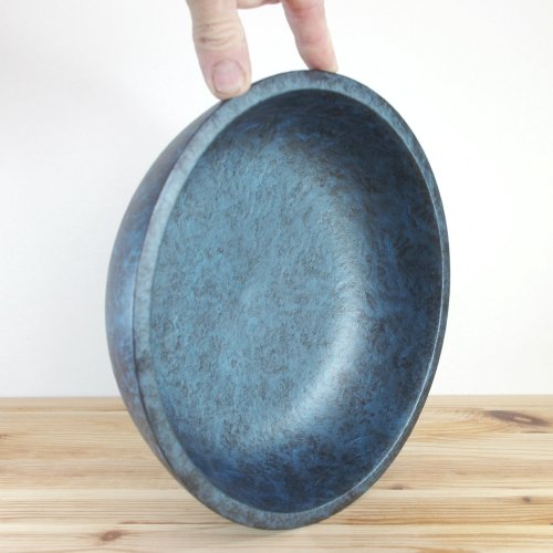 A blue wooden bowl being held up by a person's hand, placed on a wooden surface.