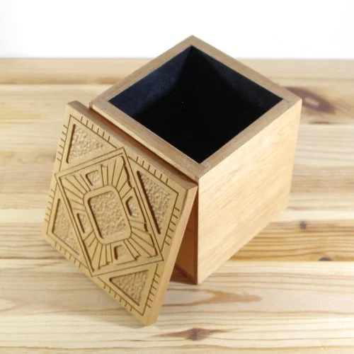 Wooden box with an intricate carved lid placed on a wooden surface.