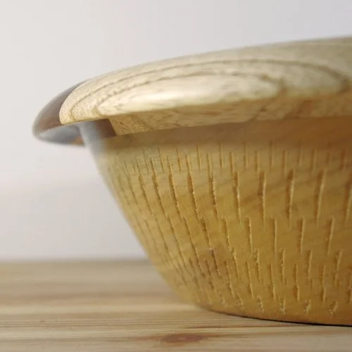 Close-up of a wooden bowl placed on a wooden surface, with a plain background.