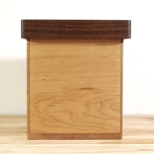 A small wooden keepsake box with a dark wood lid on a wooden surface against a white background.